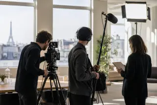 Video production crew filming in a modern office in Paris with professional equipment and Eiffel Tower visible in the background